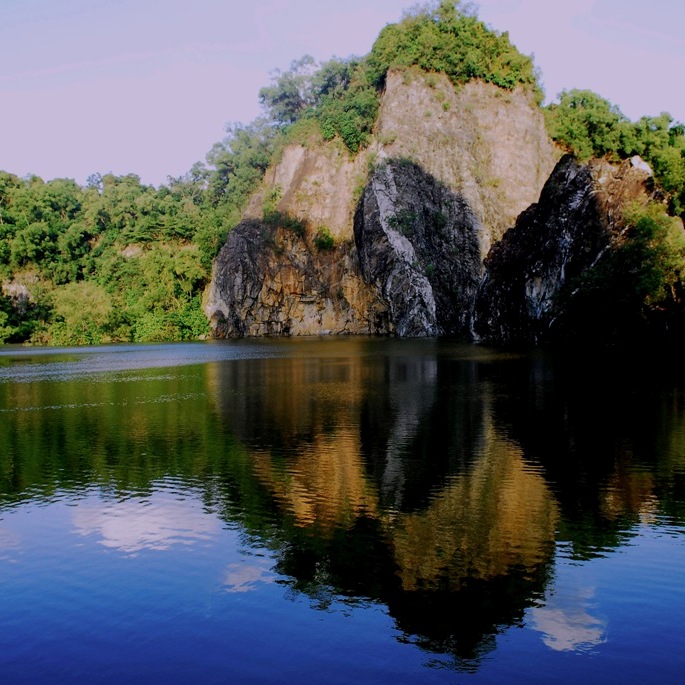 A section of the Bukit Timah Nature Reserve with some standing rock formations over the water and trees in the background